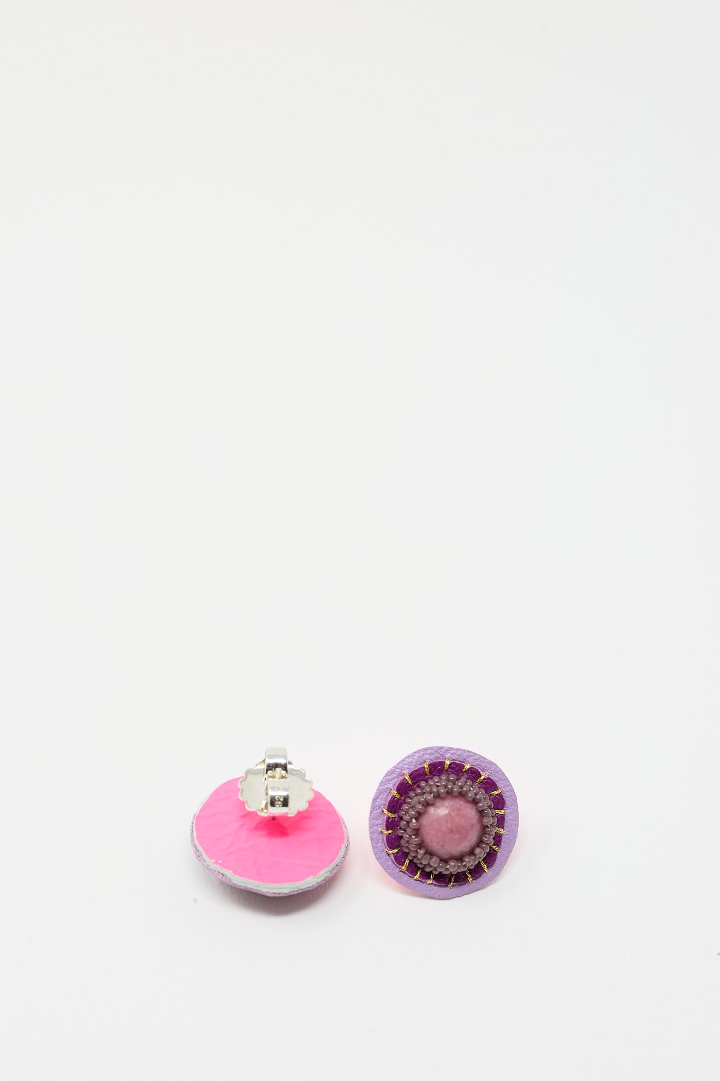 Two round, handmade earrings with intricate designs. One is pink with a silver clip, reminiscent of delicate rhodonite hues, while the other is purple with a pink center and purple beaded trim. The Stud Earrings in Rhodonite by Robin Mollicone are showcased against a white background.