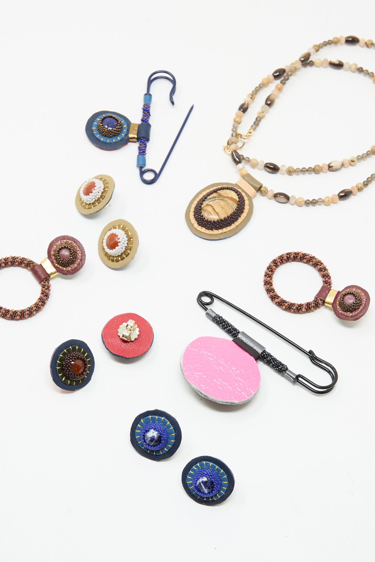 Robin Mollicone’s handmade jewelry, including Stud Earrings in Sodalite, assorted brooches, pins, and a beaded necklace with sterling silver findings, is displayed on a white background.