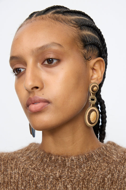 A woman with braided hair wears a brown textured sweater and large Double Stone Earrings in Picture Jasper by Robin Mollicone, glancing slightly to the side against a plain background.