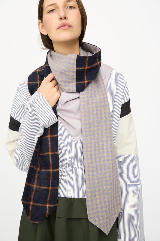 A person wearing a multicolored, patchwork-patterned shirt and the SC103 Check Wool Latch Scarf in Glossary, posing against a plain background.