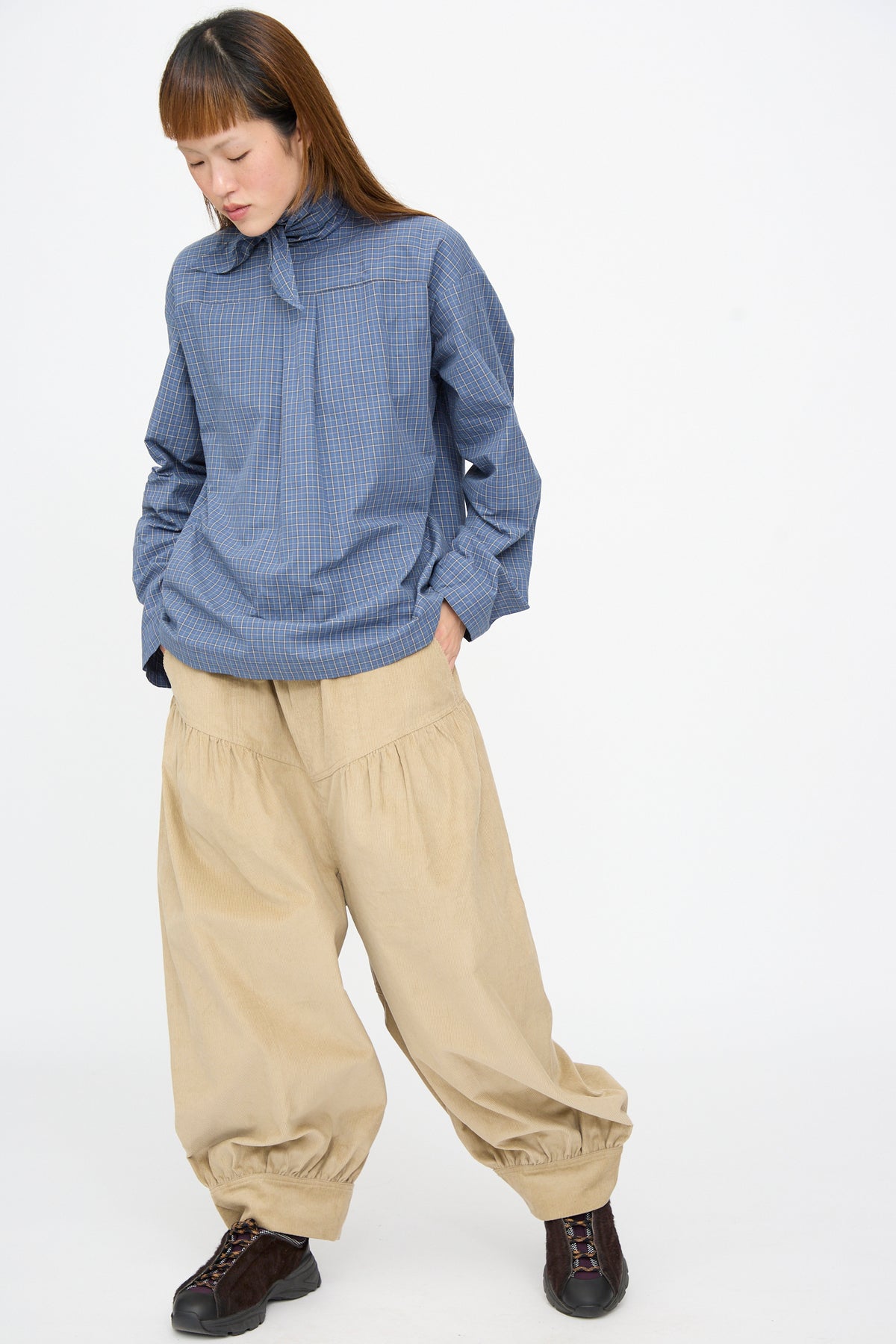 Person wearing a blue plaid long-sleeved shirt and SC103 Cotton Corduroy Crescent Pants in Wheat, featuring a loose, oversized fit with a gathered, cuffed hem.