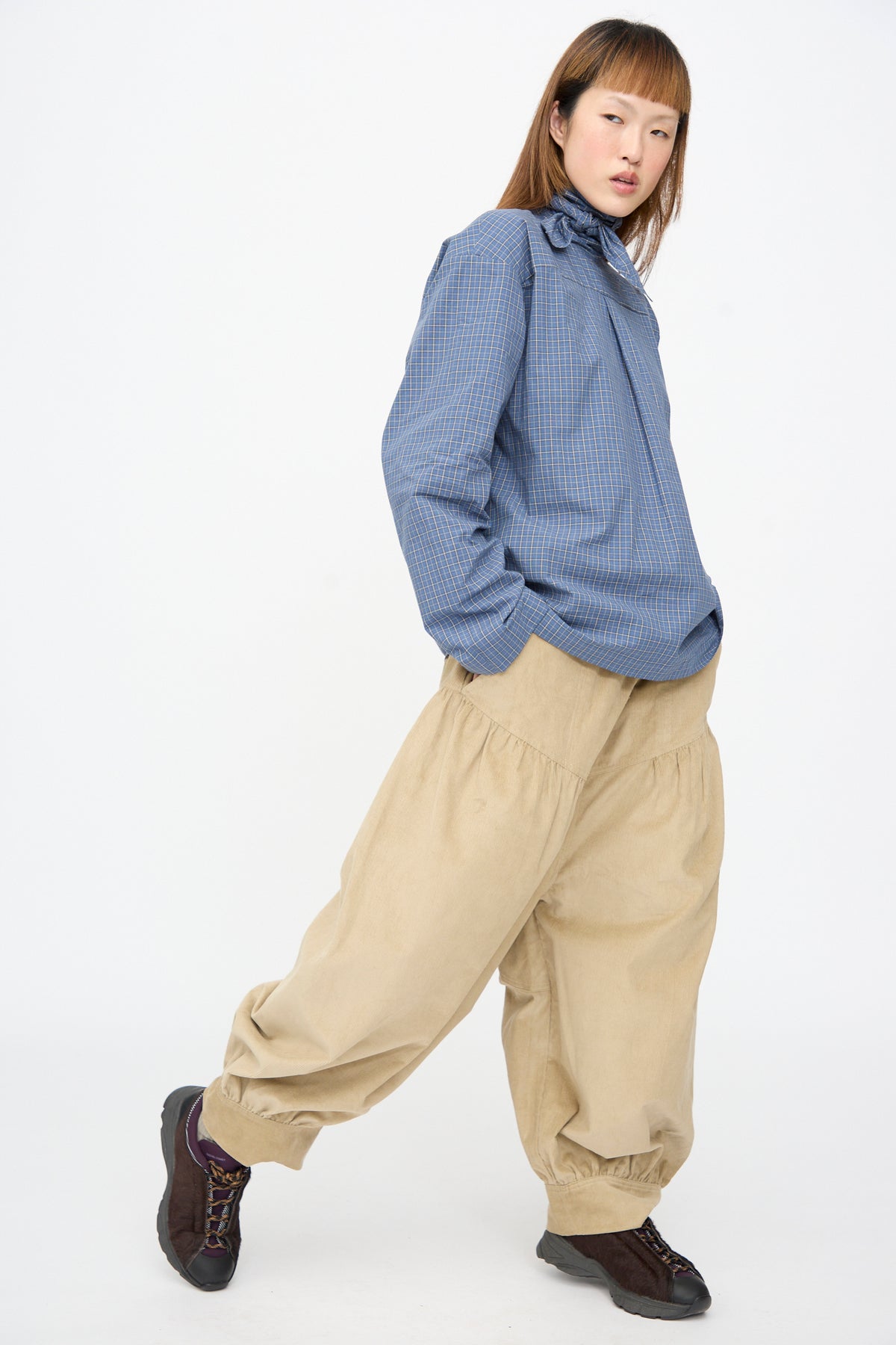 A person wearing a blue checkered long-sleeve shirt, Cotton Corduroy Crescent Pants by SC103, and dark brown sneakers.