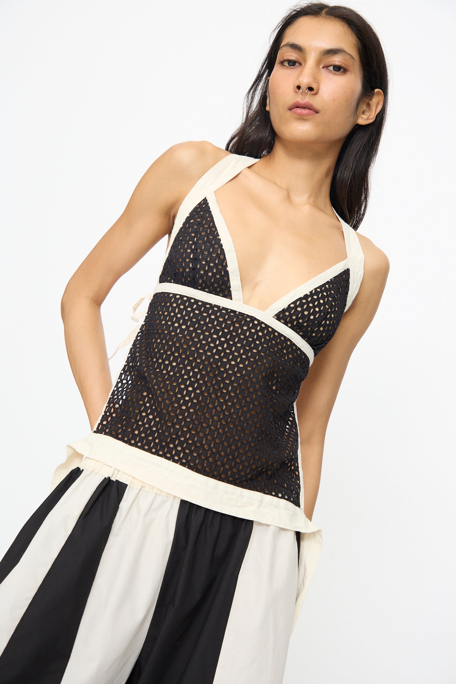 A woman wears the SC103 Cotton Eyelet Gaze Tank in Eclipse, featuring a black mesh look with white trim, paired with black-and-white wide striped pants. Made in NYC, this stylish piece stands out against a plain background.