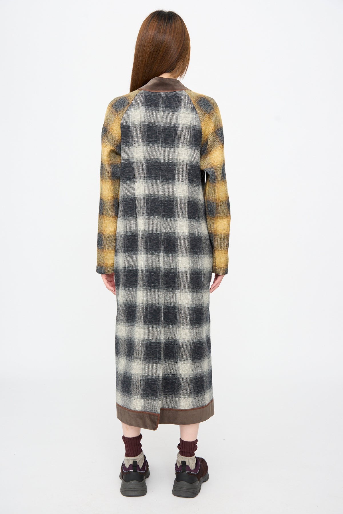 Back view of a person wearing a Cotton Flannel Frame Dress in Scholar, a long-sleeved midi dress featuring contrast sleeves and brown trim, paired with dark sneakers.