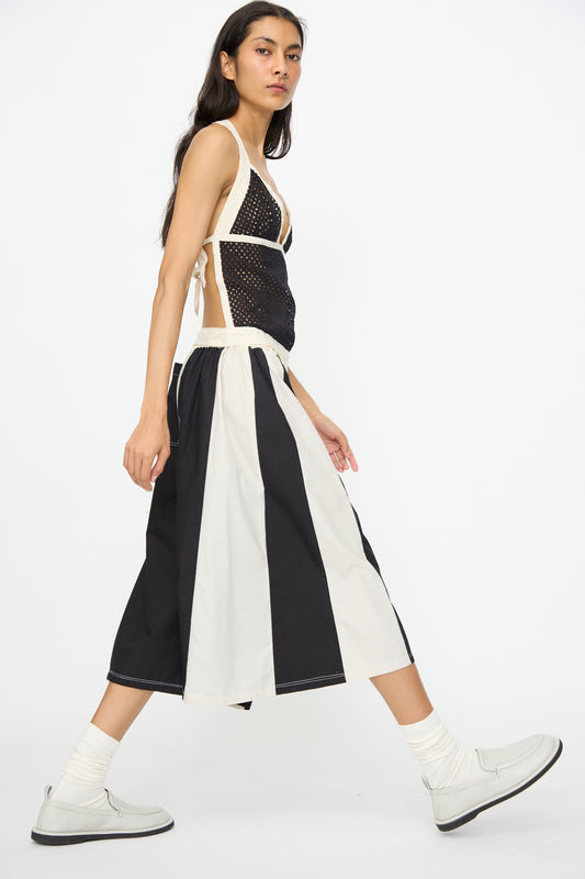 A person walks sideways in a sleeveless black mesh top, SC103 Cotton Poplin Pennant Shorts in Helix (black and white), white socks, and white shoes against a plain white background.