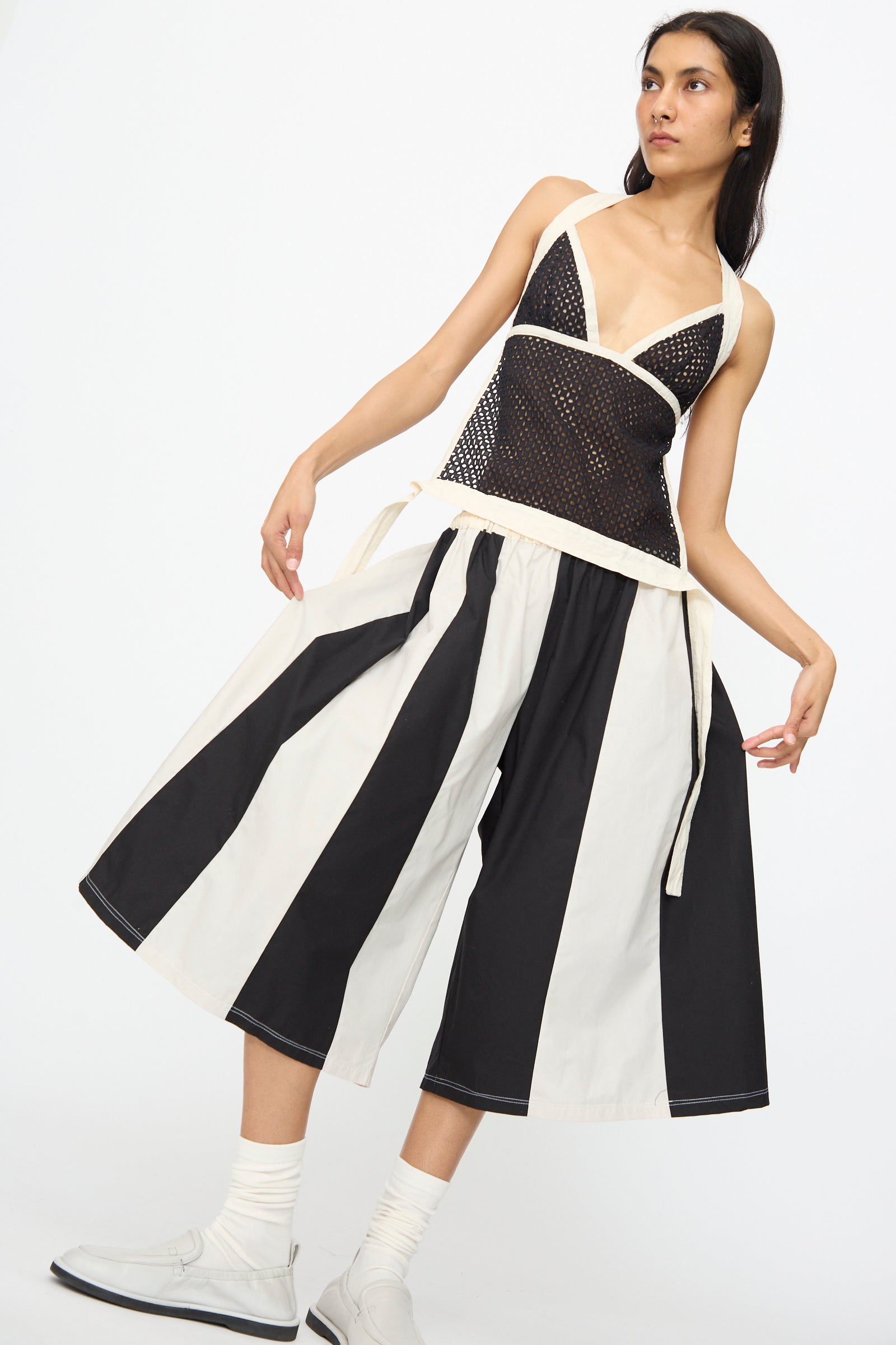 A woman poses in SC103 Cotton Poplin Pennant Shorts in Helix, featuring bold black and white stripes, styled with a black mesh halter top, white socks, and shoes against a plain white background.