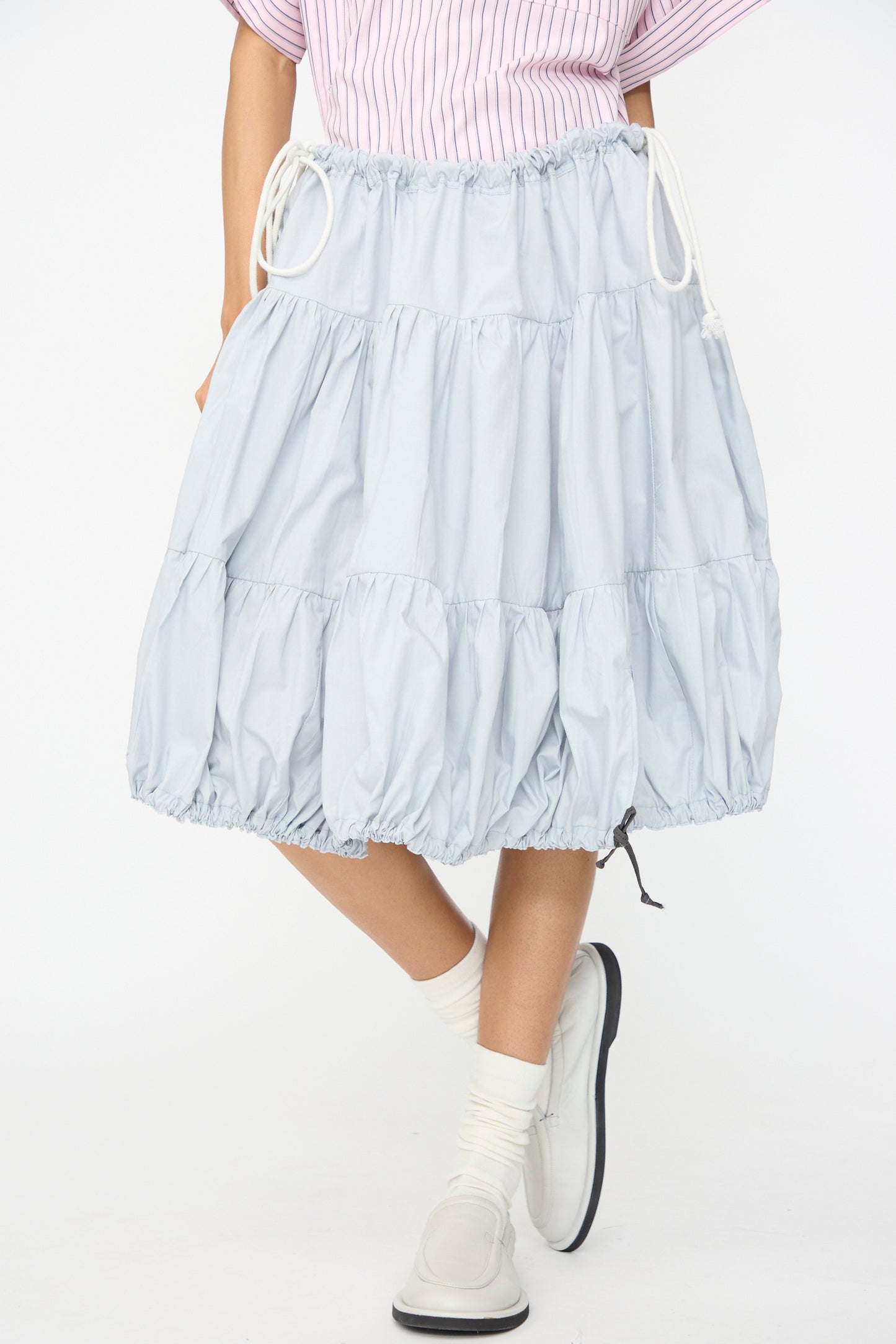 Wearing the SC103 Cotton Poplin Ramble Skirt in Sonic, paired with white socks, white shoes, and a pink striped top. Only the lower body is visible.