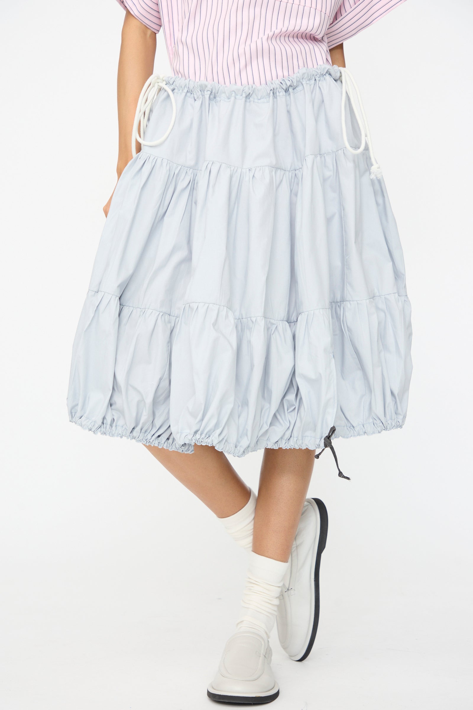 Wearing the SC103 Cotton Poplin Ramble Skirt in Sonic, paired with white socks, white shoes, and a pink striped top. Only the lower body is visible.