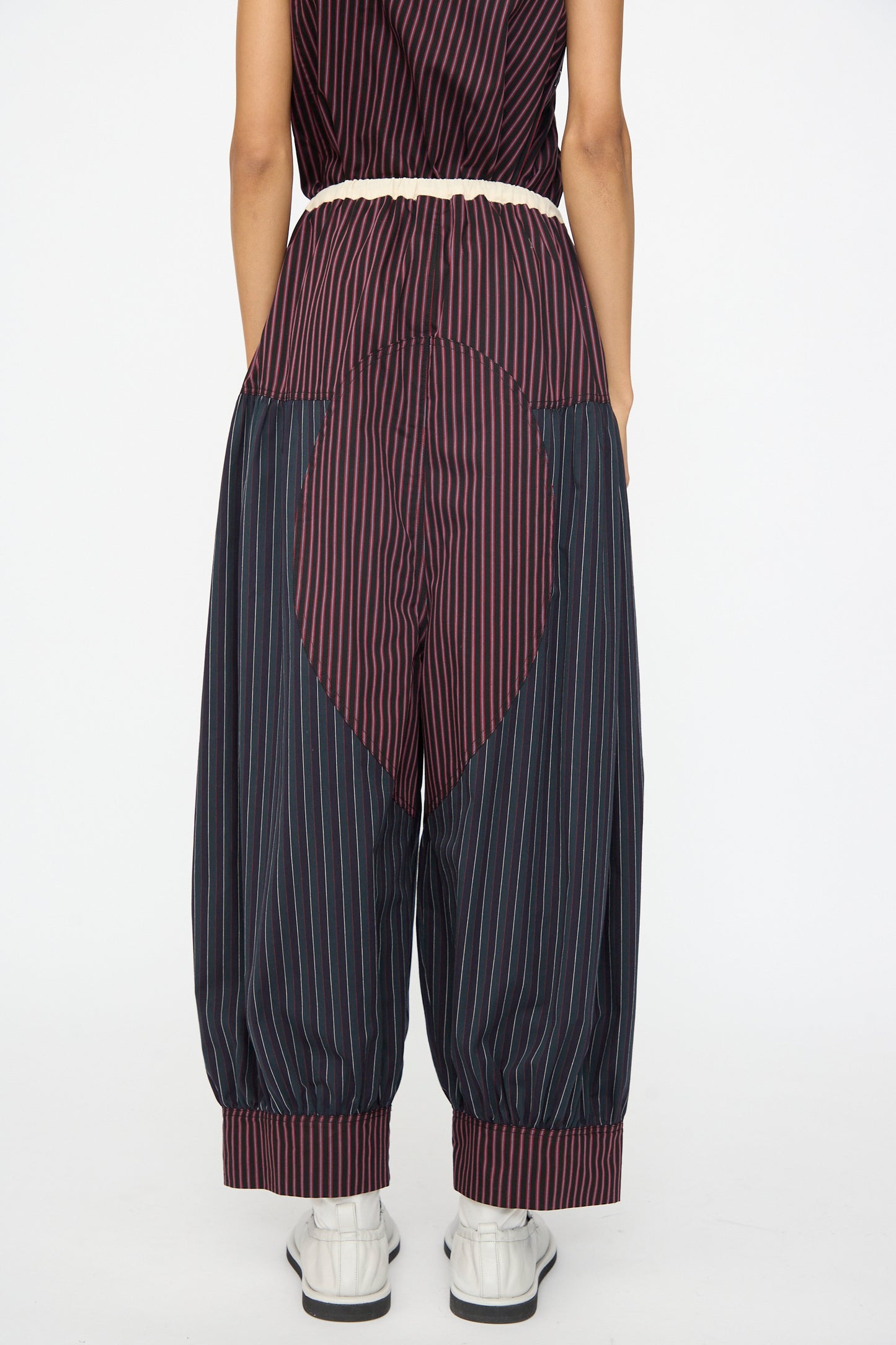 A person stands with their back to the camera, wearing SC103 Cotton Suiting Crescent Pants in Celestine Stripe, featuring a heart-shaped seat panel, paired with white shoes.
