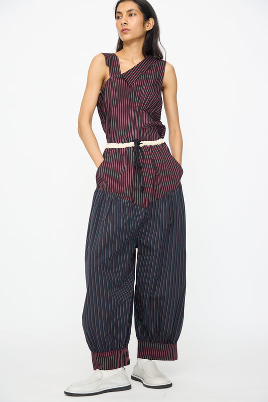 Person stands against a white background wearing SC103's Cotton Suiting Crescent Pants in Celestine Stripe, styled with a sleeveless striped cotton top, white belt, and white shoes.