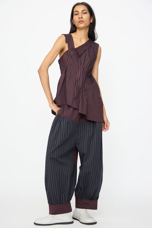 A person wears the SC103 Cotton Suiting Solstice Top in Celestine Stripe—an asymmetrical, sleeveless striped cotton piece—paired with loose striped pants and light shoes, set against a plain background. This look is thoughtfully made in NYC.