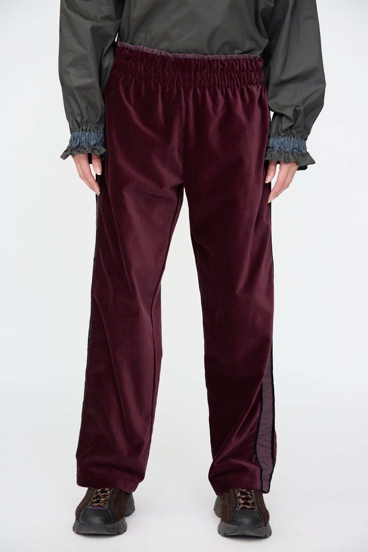 SC103 Cotton Velvet Chord Pants in Noble, deep purple cotton velvet with a gathered elastic waistband and side stripes, paired with sneakers.