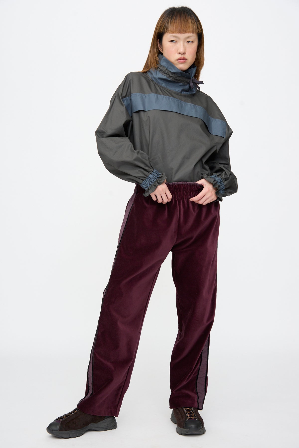 A person wearing a grey pullover and Cotton Velvet Chord Pants in Noble, featuring side stripes, paired with dark sneakers.