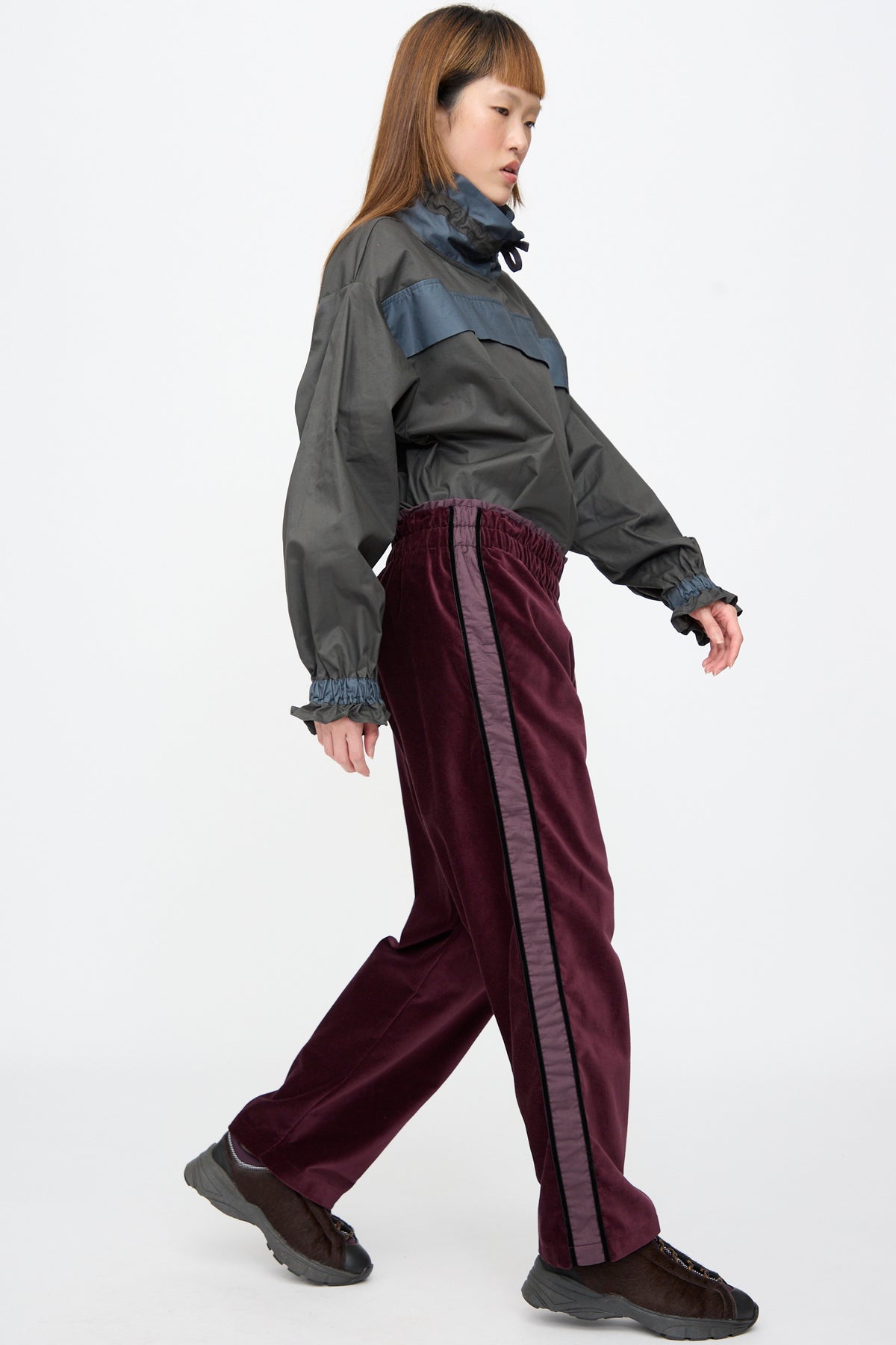 A person wearing a grey pullover jacket and Cotton Velvet Chord Pants in Noble, a deep purple pant with a stripe down the leg.
