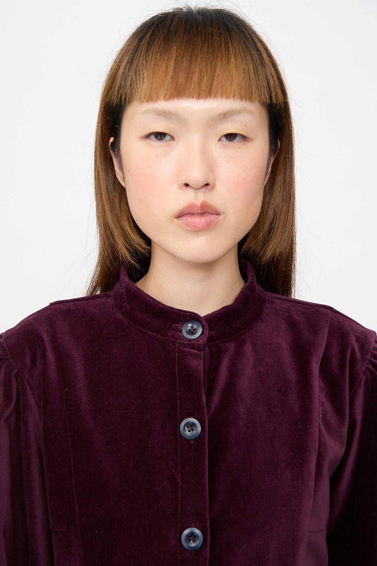 A model wearing a deep purple Cotton Velvet Index Dress in Noble, a button-front mini dress with a mandarin collar and balloon sleeves.