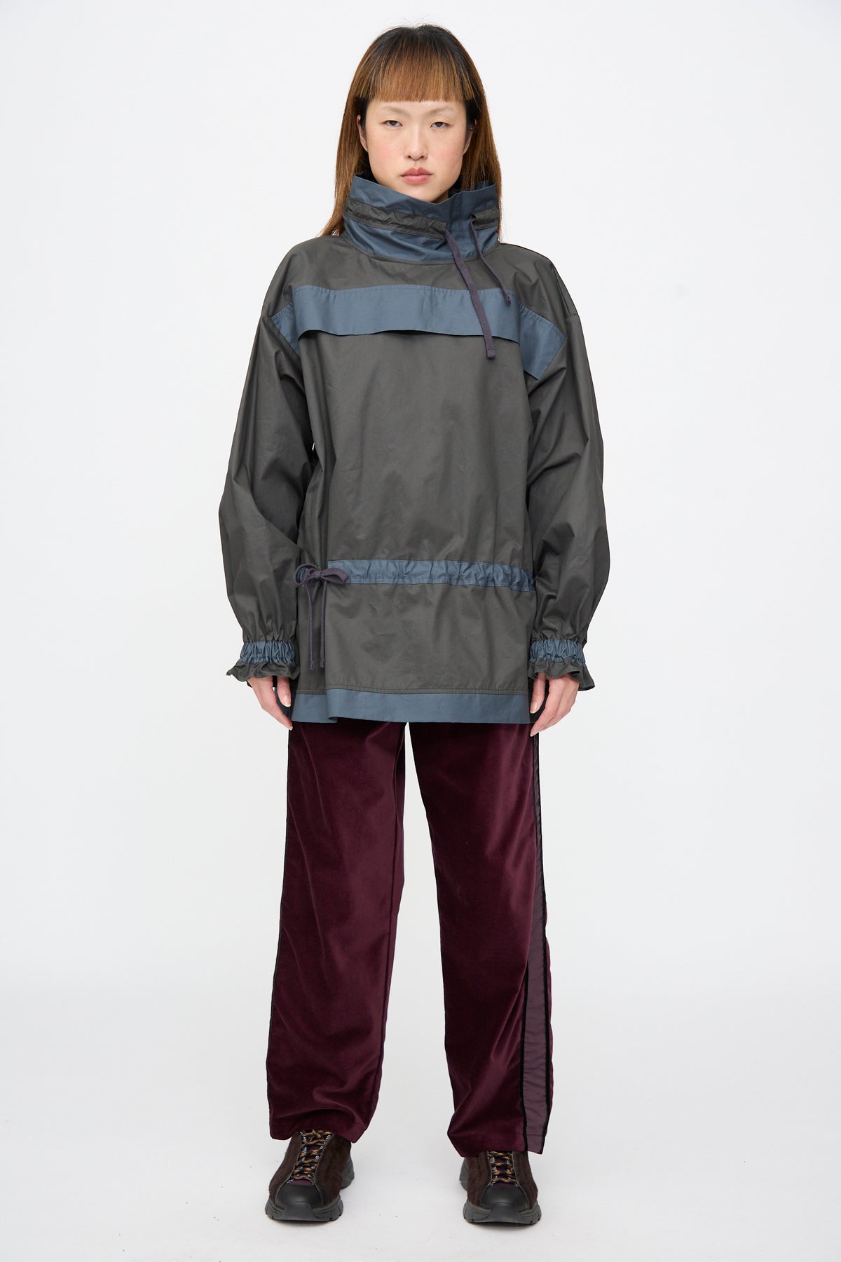 A model wears the SC103 Crisp Cotton Incline Tunic in Twilight, a two-tone grey and blue tunic with a high collar and drawstring waist, paired with dark maroon trousers and sneakers.