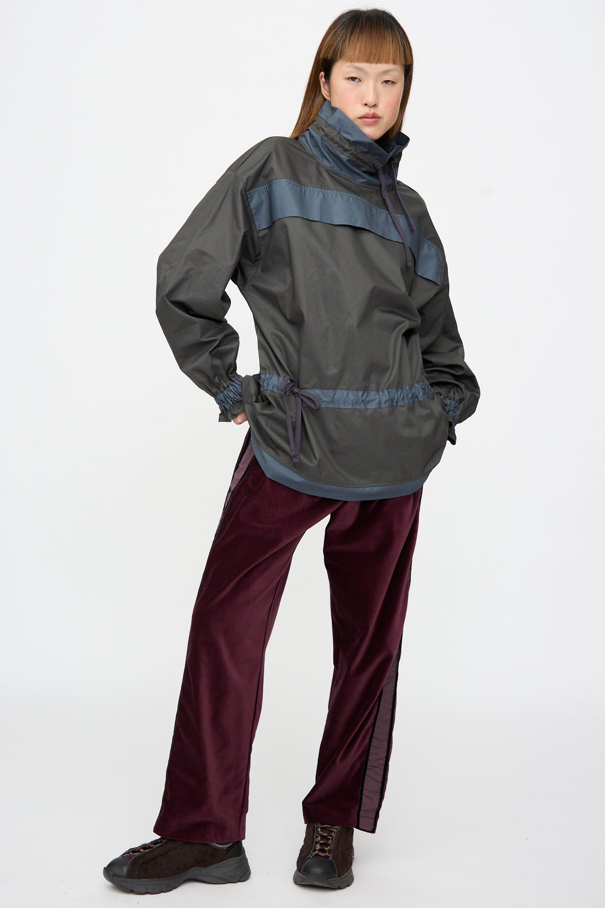 A person wears a charcoal grey, high-neck Crisp Cotton Incline Tunic in Twilight with a drawstring waist and dark maroon, relaxed fit wide-leg trousers.