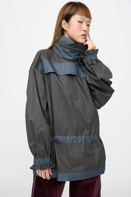 A person wearing a relaxed-fit, dark grey Crisp Cotton Incline Tunic in Twilight with blue trim and gathered cuffs.