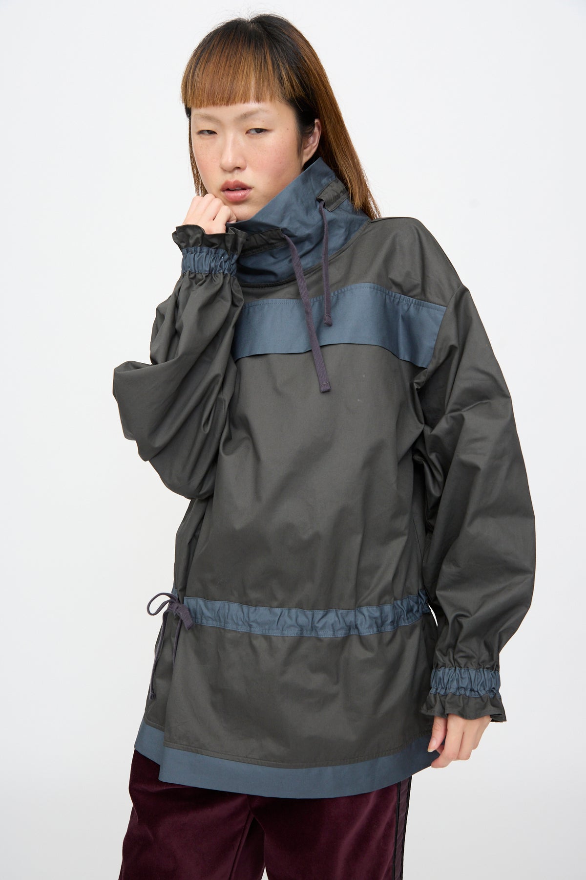 A person wears an SC103 Crisp Cotton Incline Tunic in Twilight, a two-tone dark gray cotton tunic with a high collar, drawstring waist, and contrasting blue bands across the chest, waist, and hem.