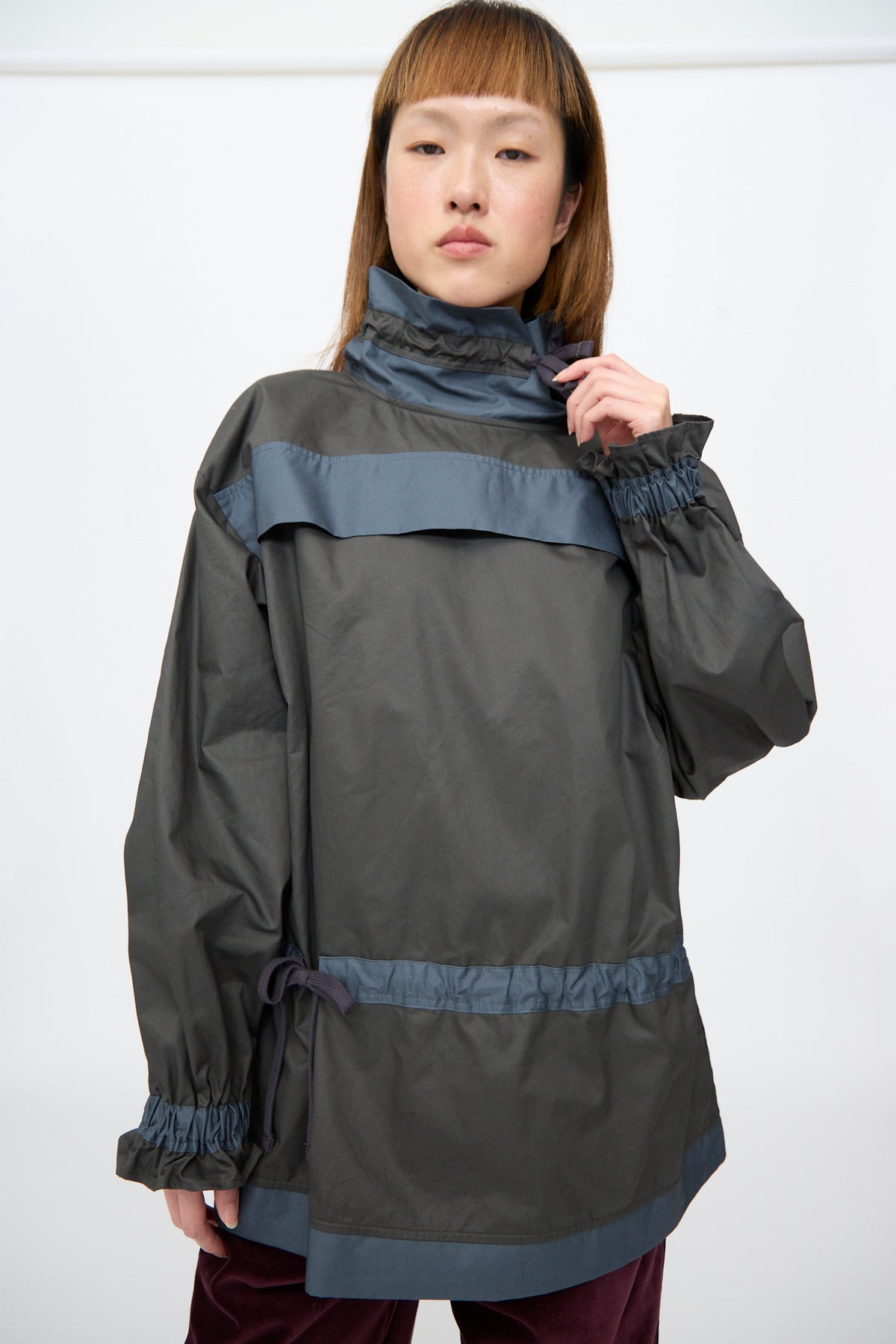 A person wearing the SC103 Crisp Cotton Incline Tunic in Twilight, a relaxed fit, dark grey cinched tunic with a high collar, gathered cuffs, and horizontal blue bands across the chest and waist.