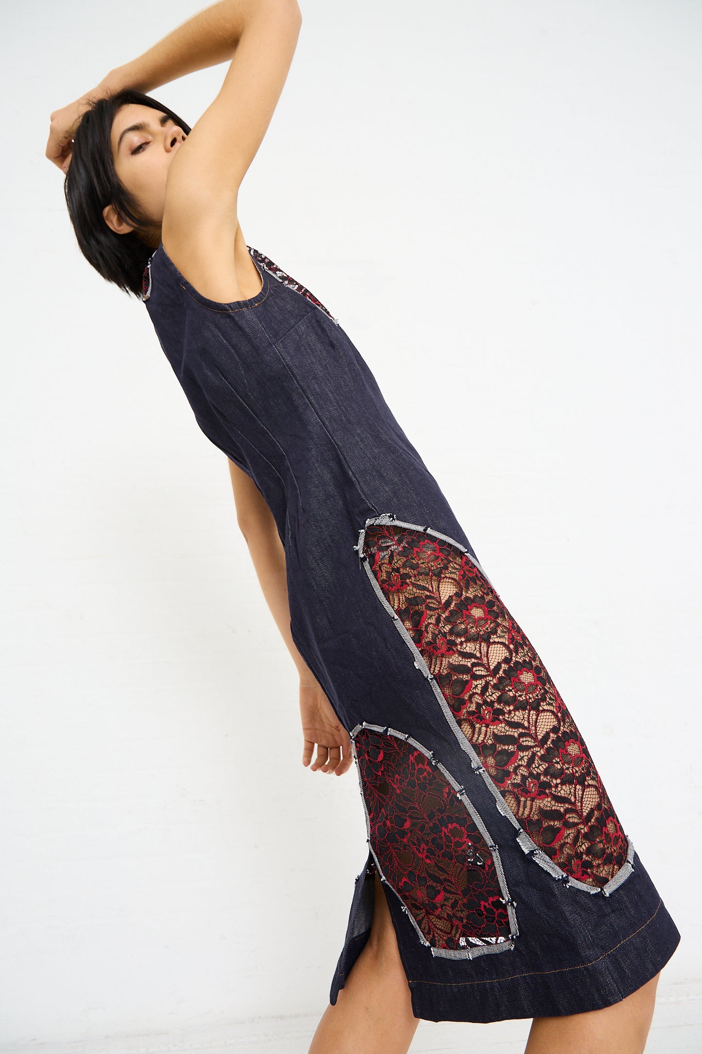 A woman posing in a sleeveless SC103 Denim Motto Dress in Weft with a red patterned inset and cutout lace detailing, against a white background.