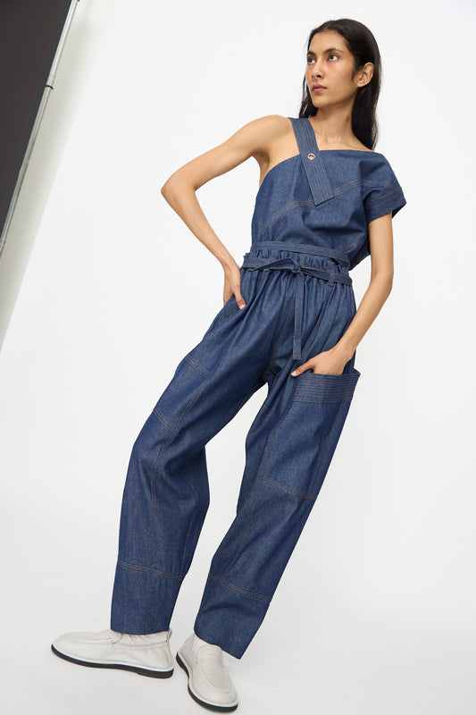 A woman stands against a white background wearing SC103’s Denim Vault Pants in Soft Indigo, featuring a relaxed fit and wide legs, paired with white shoes.