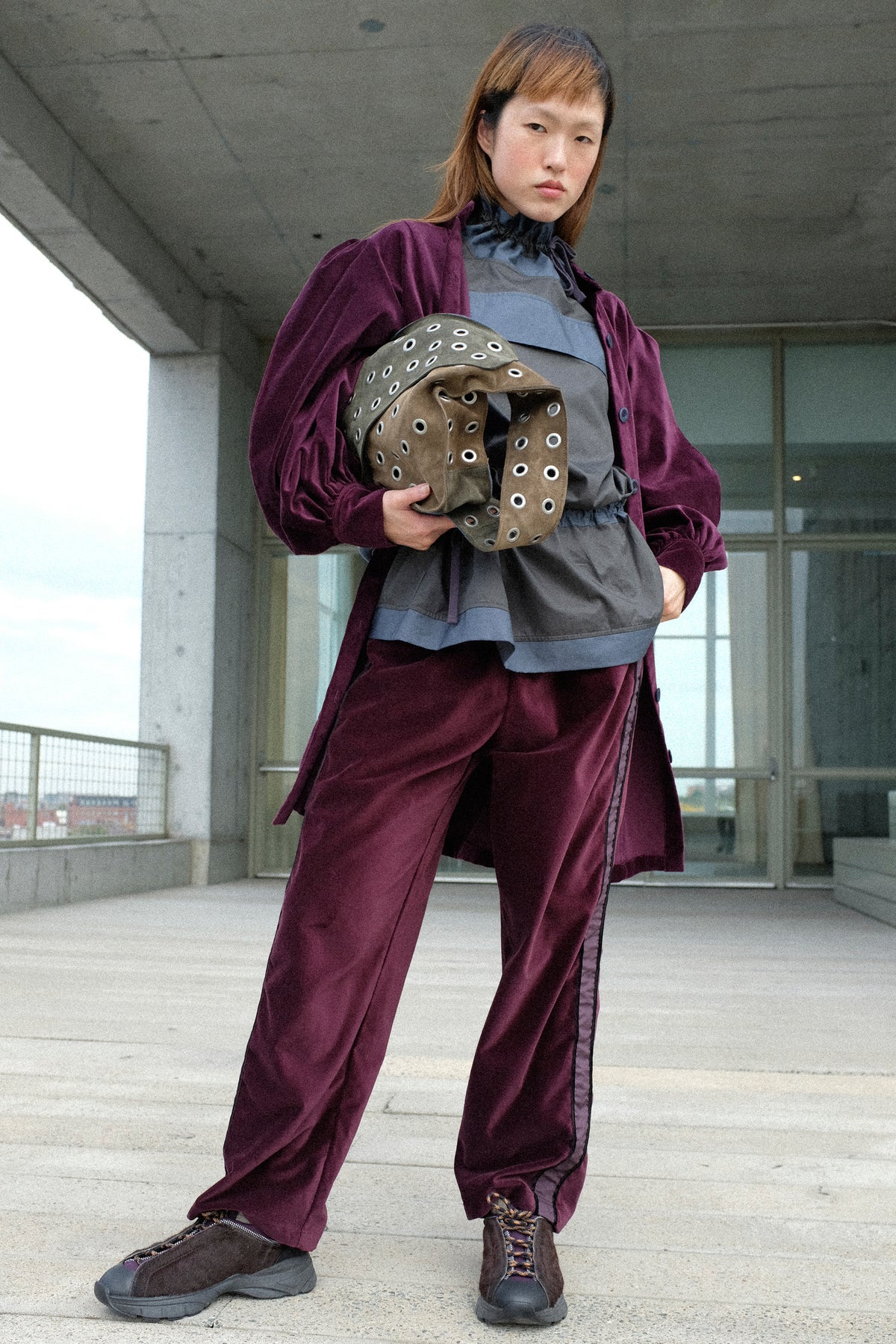 A woman standing outside holding an SC103 bag wearing the Cotton Velvet Index Dress in Noble, Crisp Cotton Incline Tunic in Twilight, Cotton Velvet Chord Pants in Noble.