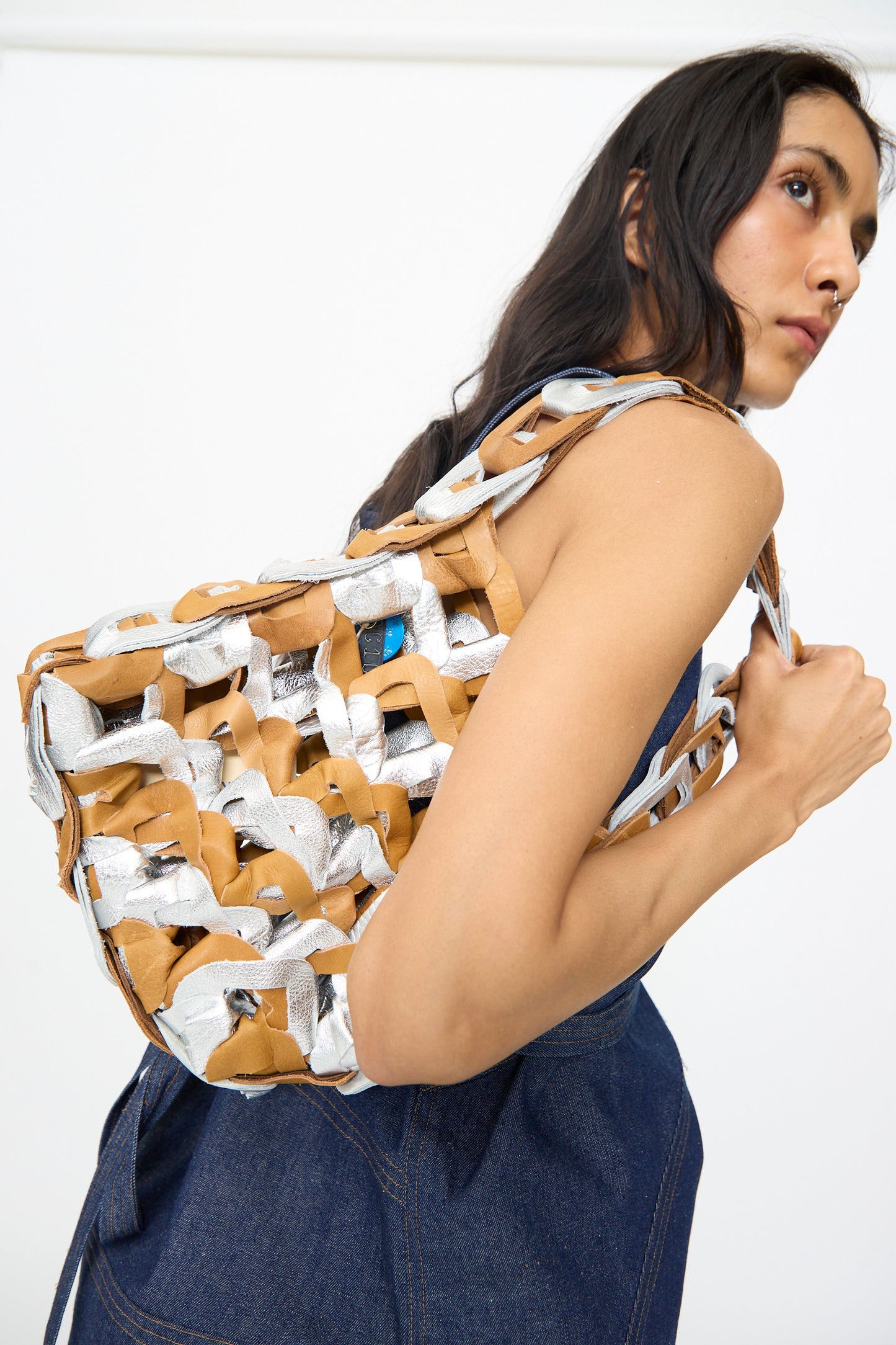 A person carries the SC103 Leather Links Tote in Parcel—a large, handmade bag featuring interlocking leather and metallic silver details—over their shoulder.