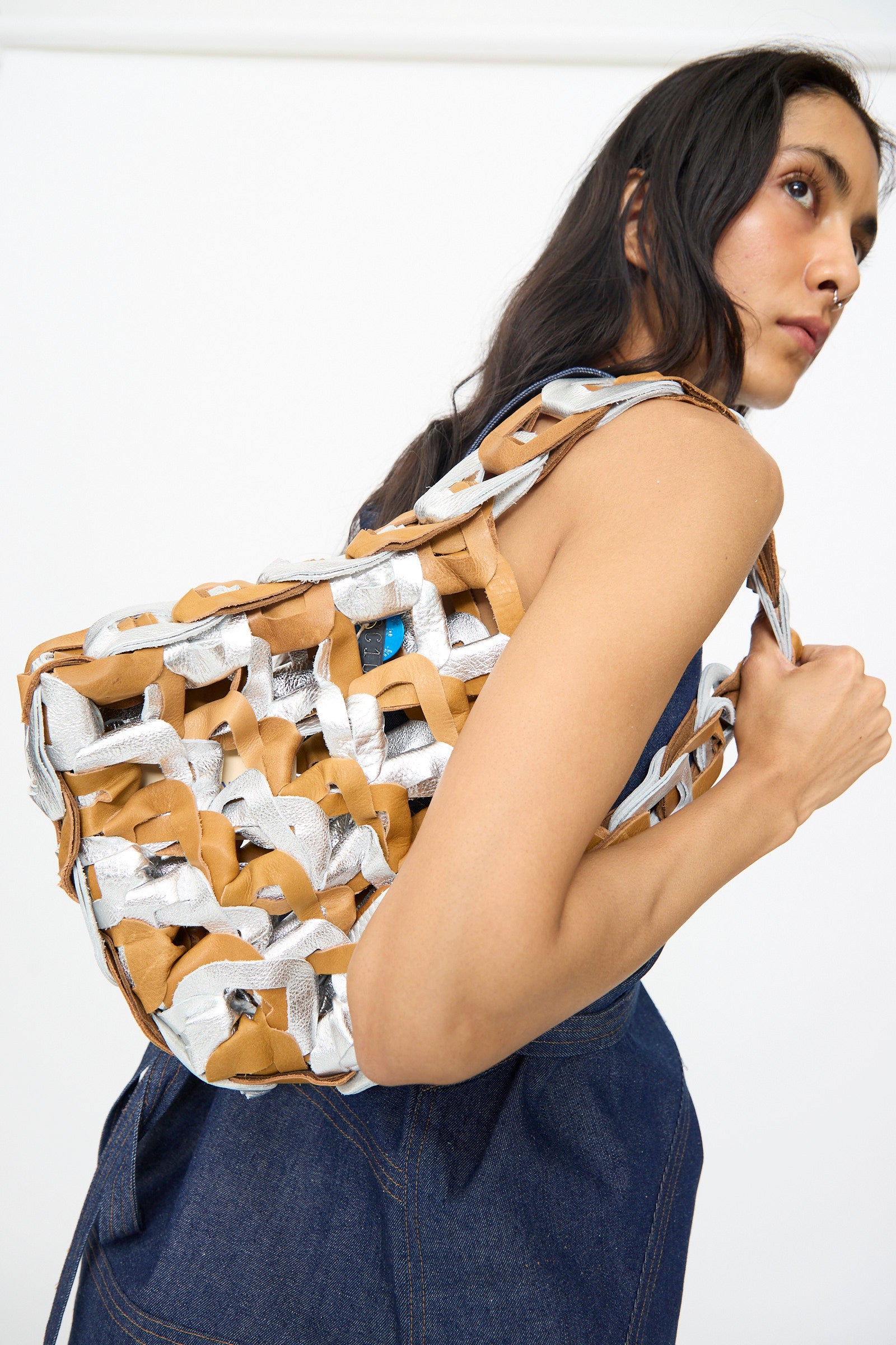 A person carries the SC103 Leather Links Tote in Parcel—a large, handmade bag featuring interlocking leather and metallic silver details—over their shoulder.