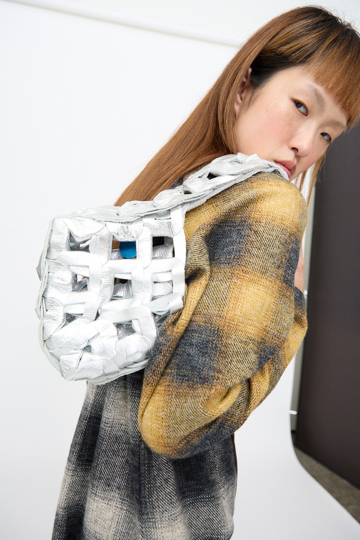 A person in a plaid jacket carries a small, metallic silver Leather Links Tote Mini, featuring interlocking leather links.
