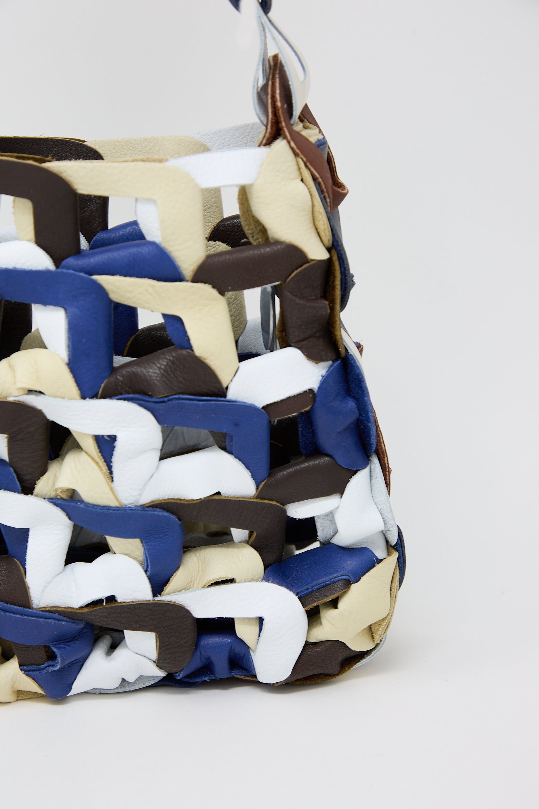 Close-up of a SC103 Leather Links Tote in Quill with interwoven leather strips in blue, white, and brown colors, against a neutral background.