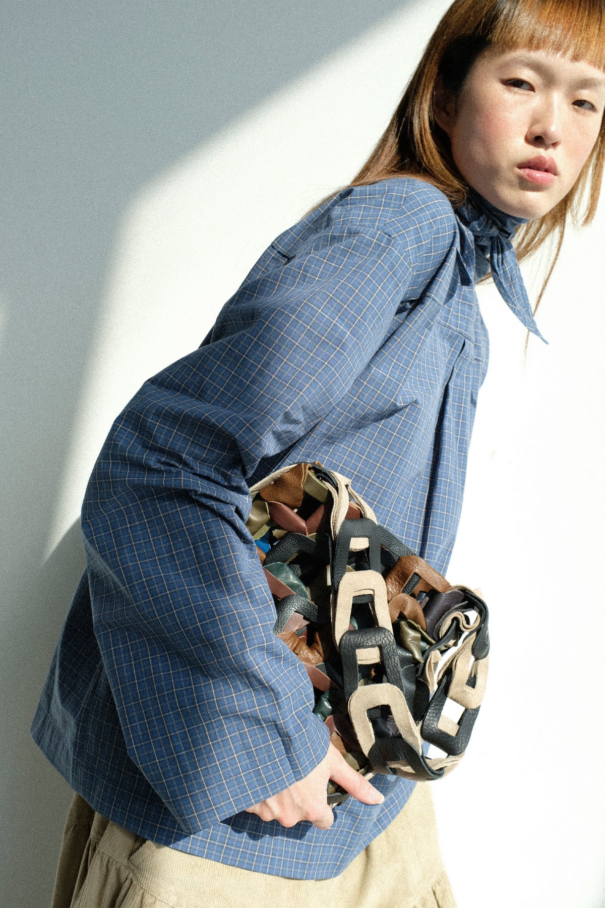 A woman holding SC103's Links Tote, wearing the Plaid Poplin Compass Blouse in Aerial.