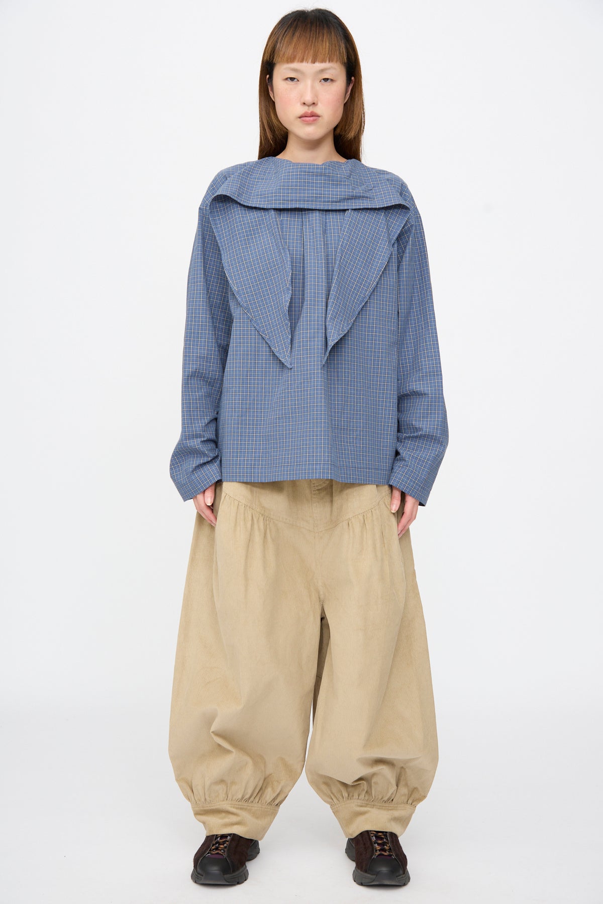 Person wearing a Plaid Poplin Compass Blouse in Aerial with neck tie undone, paired with beige wide-leg cuffed trousers and dark sneakers.