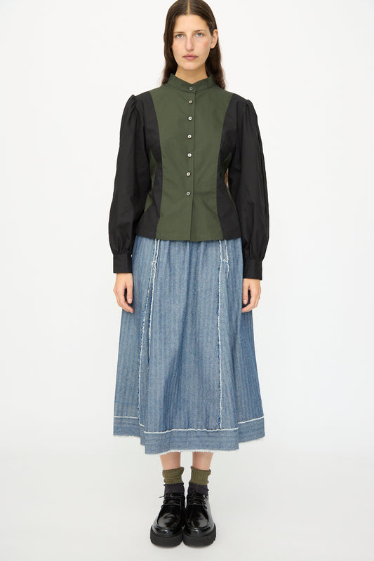 A woman faces forward against a white background, wearing the SC103 Poplin Folio Blouse in Bolt, a blue denim midi skirt, green socks, and black shoes.