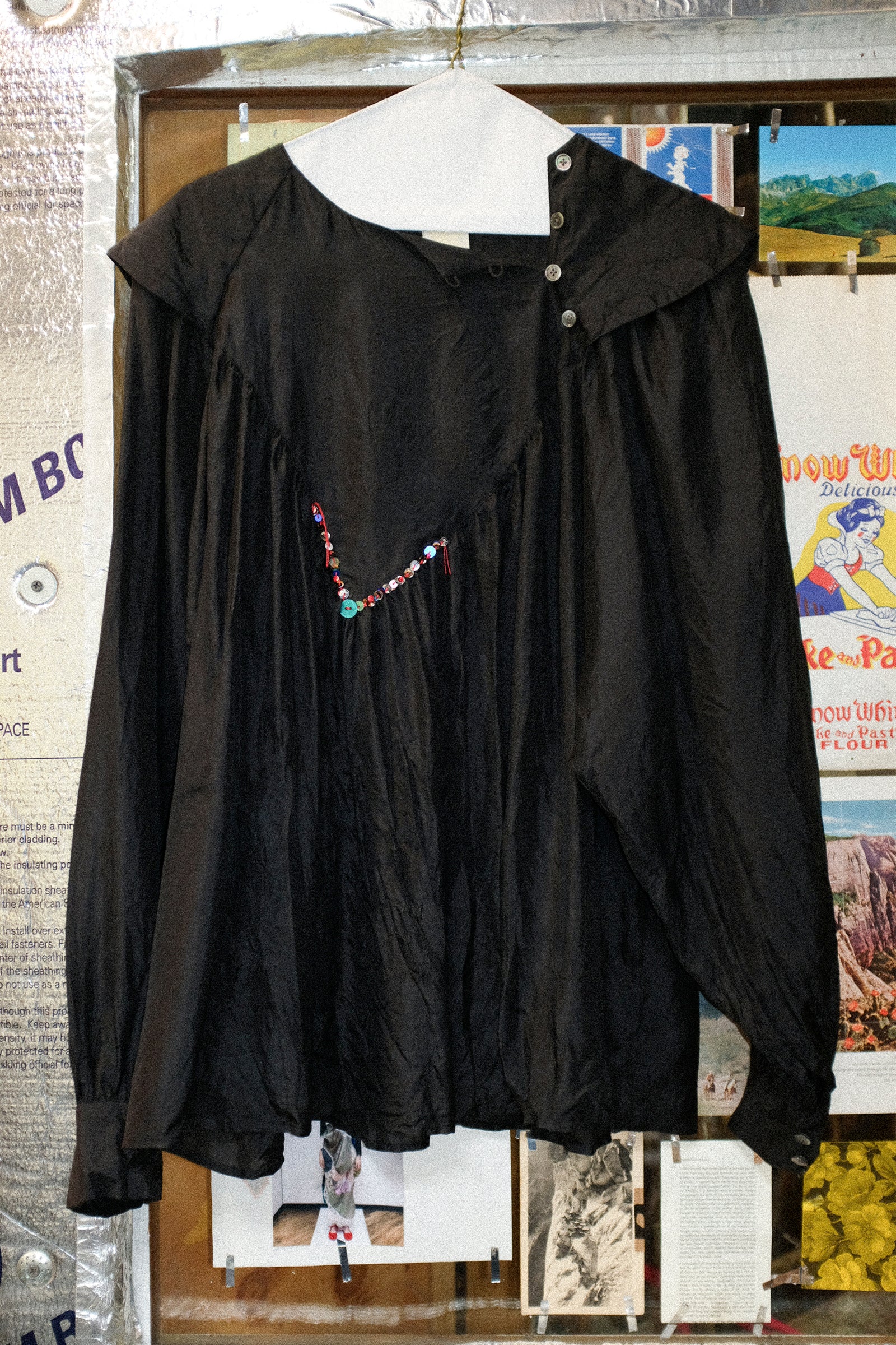SC103'S Silk Prince Blouse on a hanger against a textured wall.