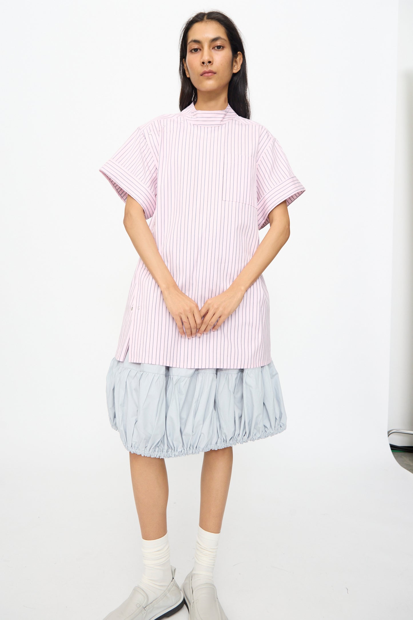 A person stands against a white background wearing the SC103 Stripe Cotton Wish Top in Blushline, paired with a light blue gathered skirt, white socks, and light-colored shoes.