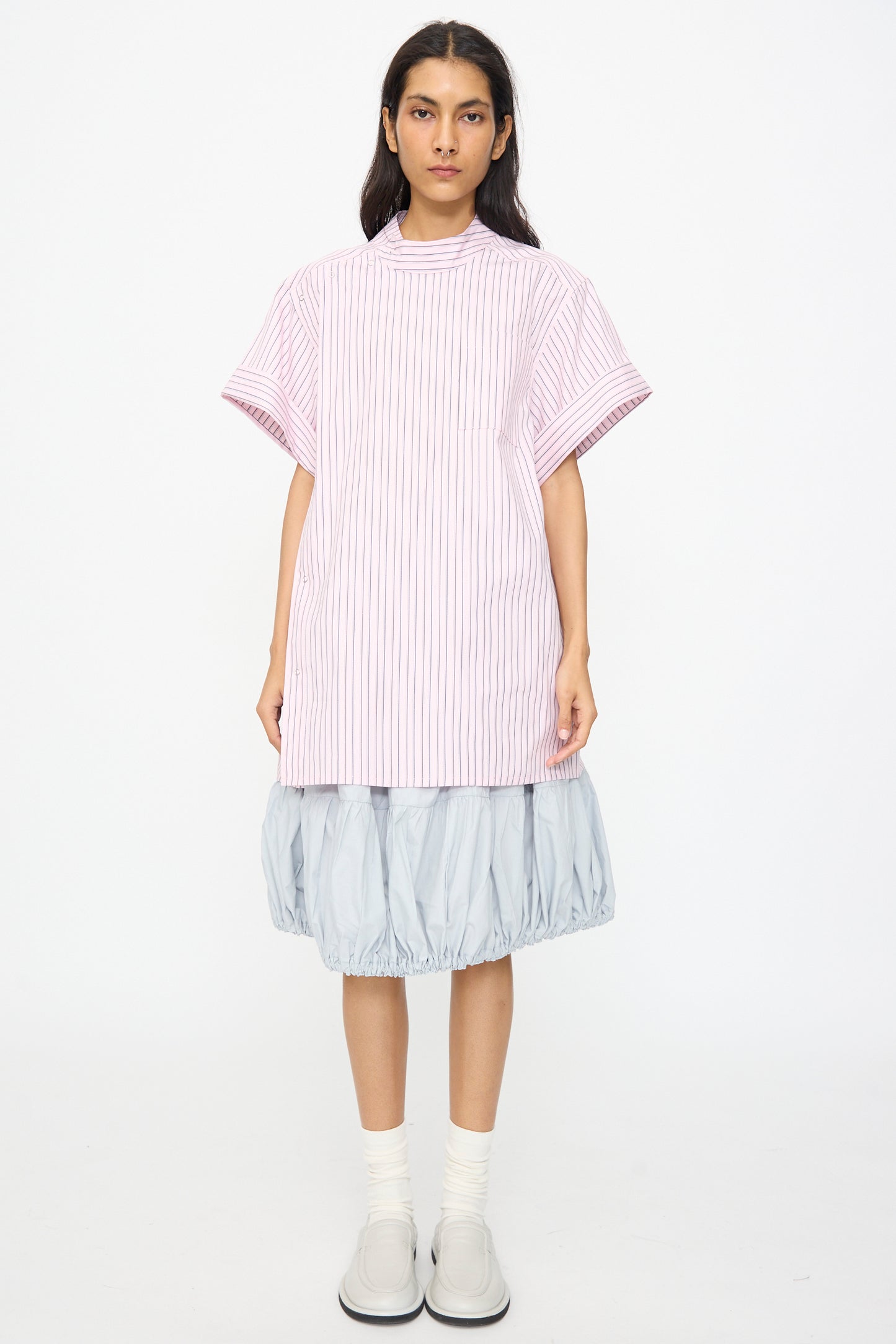 A person stands facing forward in a SC103 Stripe Cotton Wish Top in Blushline, a light blue balloon skirt, white socks, and light gray shoes against a plain white background.