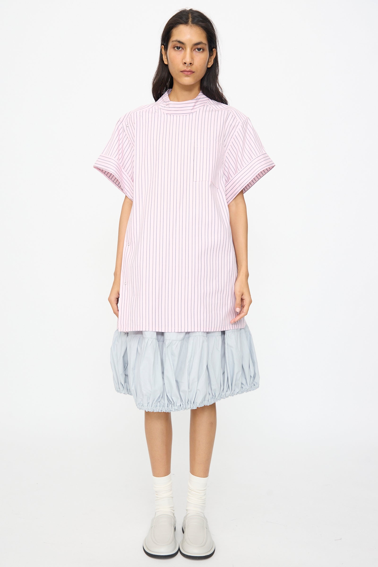 A person stands facing forward in a SC103 Stripe Cotton Wish Top in Blushline, a light blue balloon skirt, white socks, and light gray shoes against a plain white background.