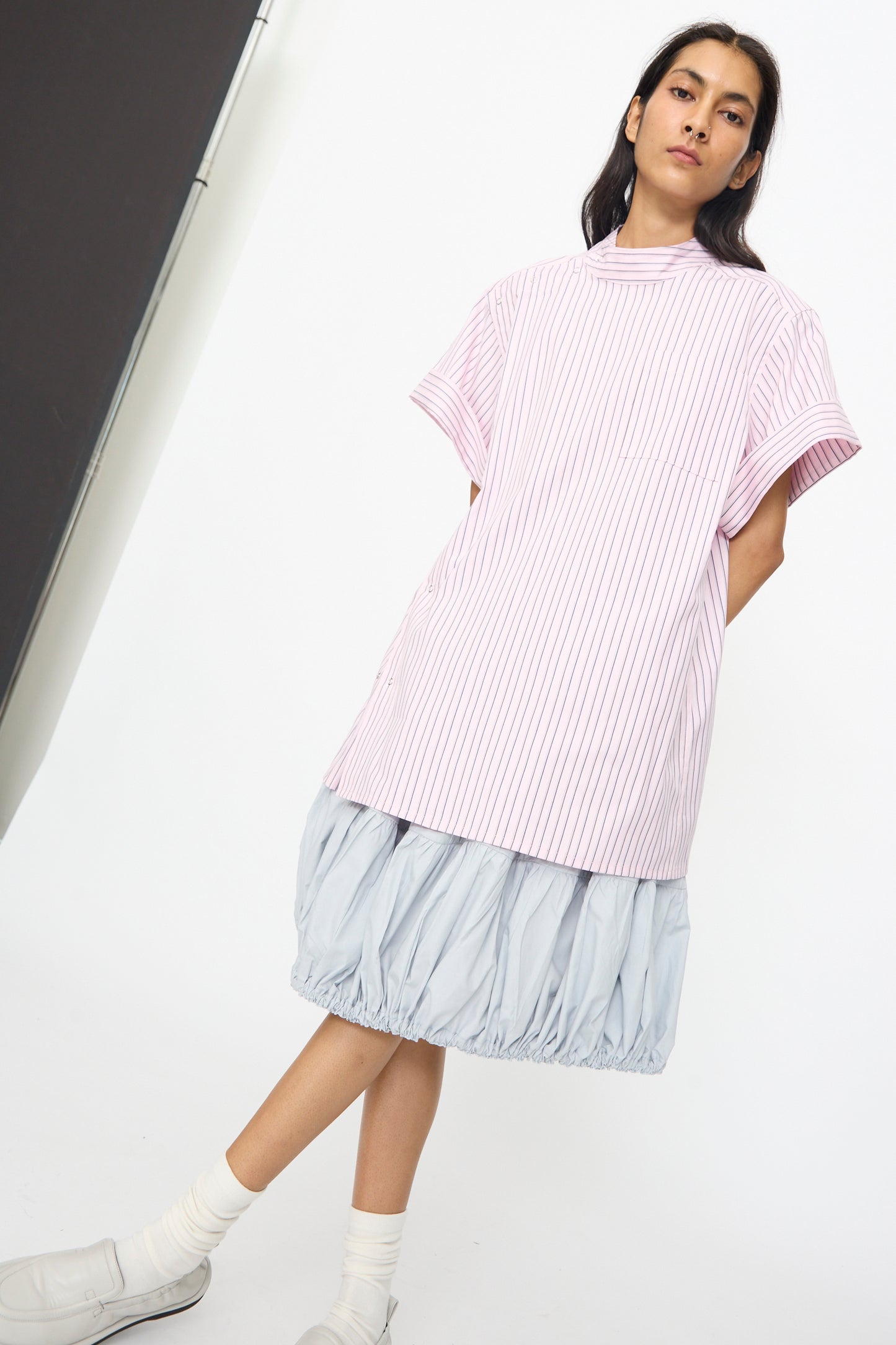 A person stands against a white background wearing the SC103 Stripe Cotton Wish Top in Blushline over a light blue skirt, paired with white socks and shoes.