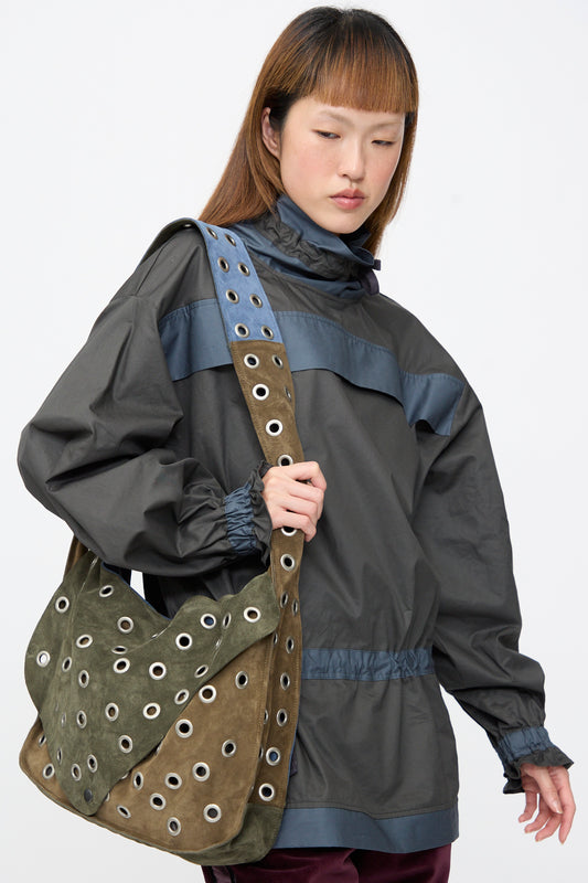 A person wears a large patchwork Suede Leather Record Messenger in Abyss with metal eyelets on the strap and body.