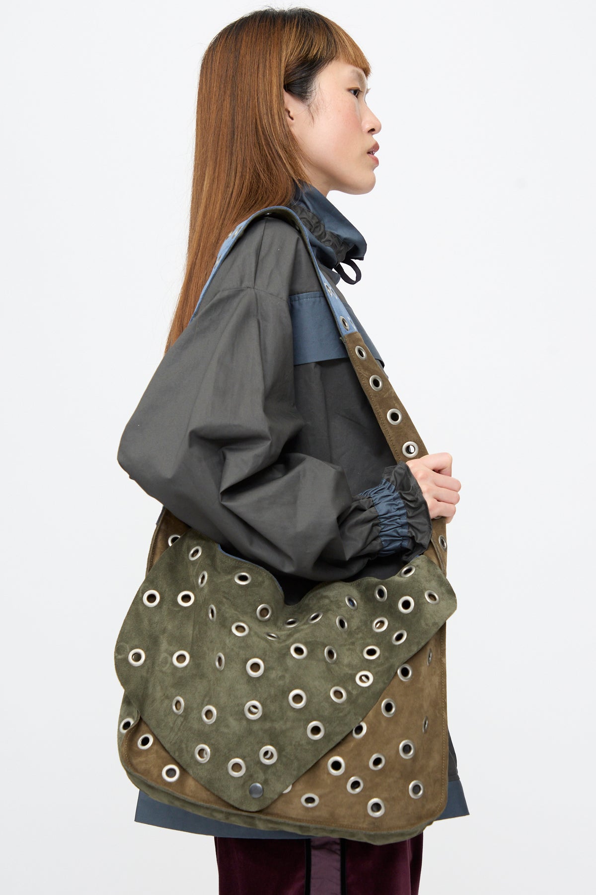 A person wearing a Suede Leather Record Messenger, a patchwork bag covered in silver metal grommets.