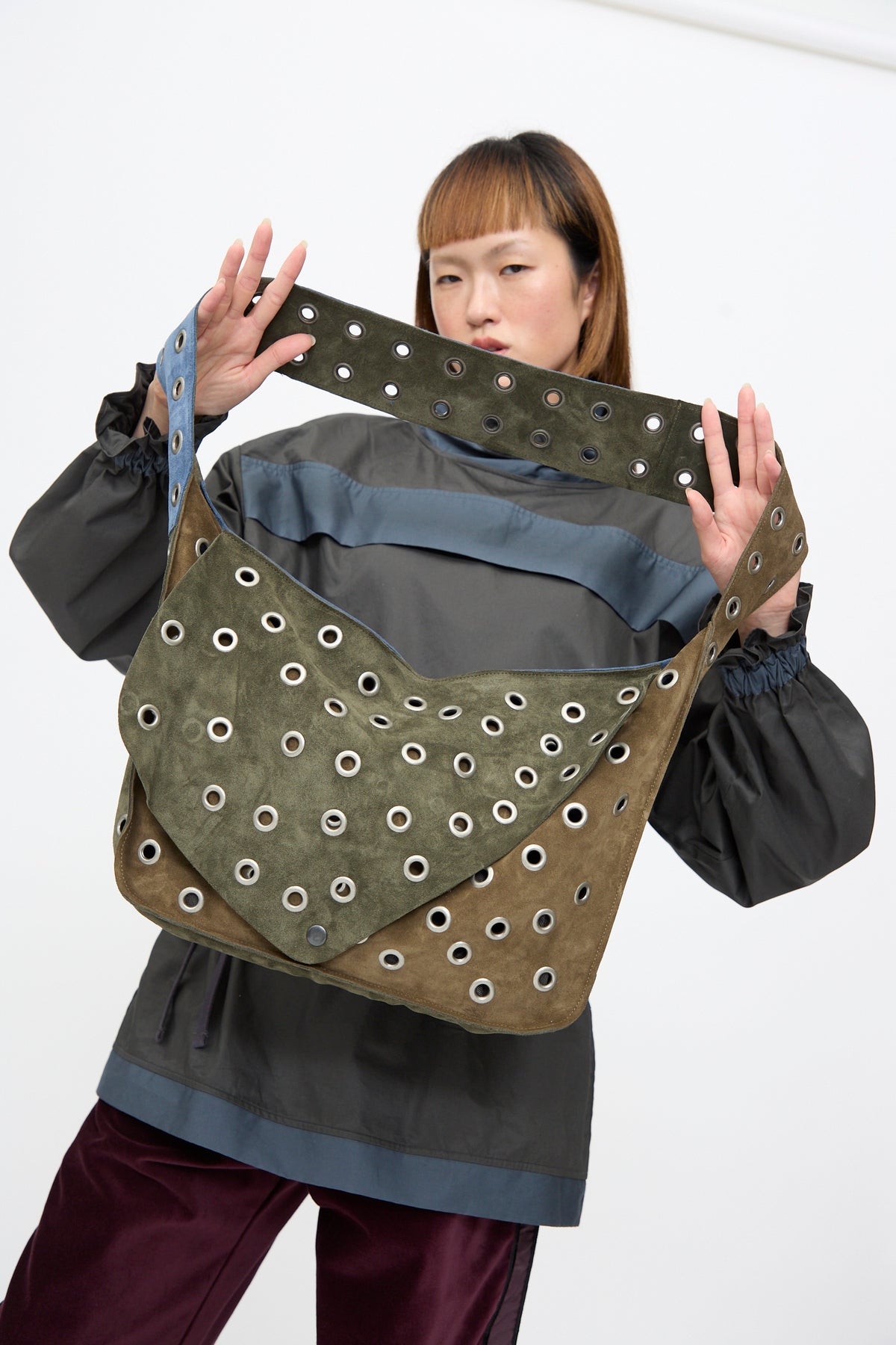 Person holds up the multi-colored SC103 Suede Leather Record Messenger in Abyss featuring silver metal grommets across the body and strap.