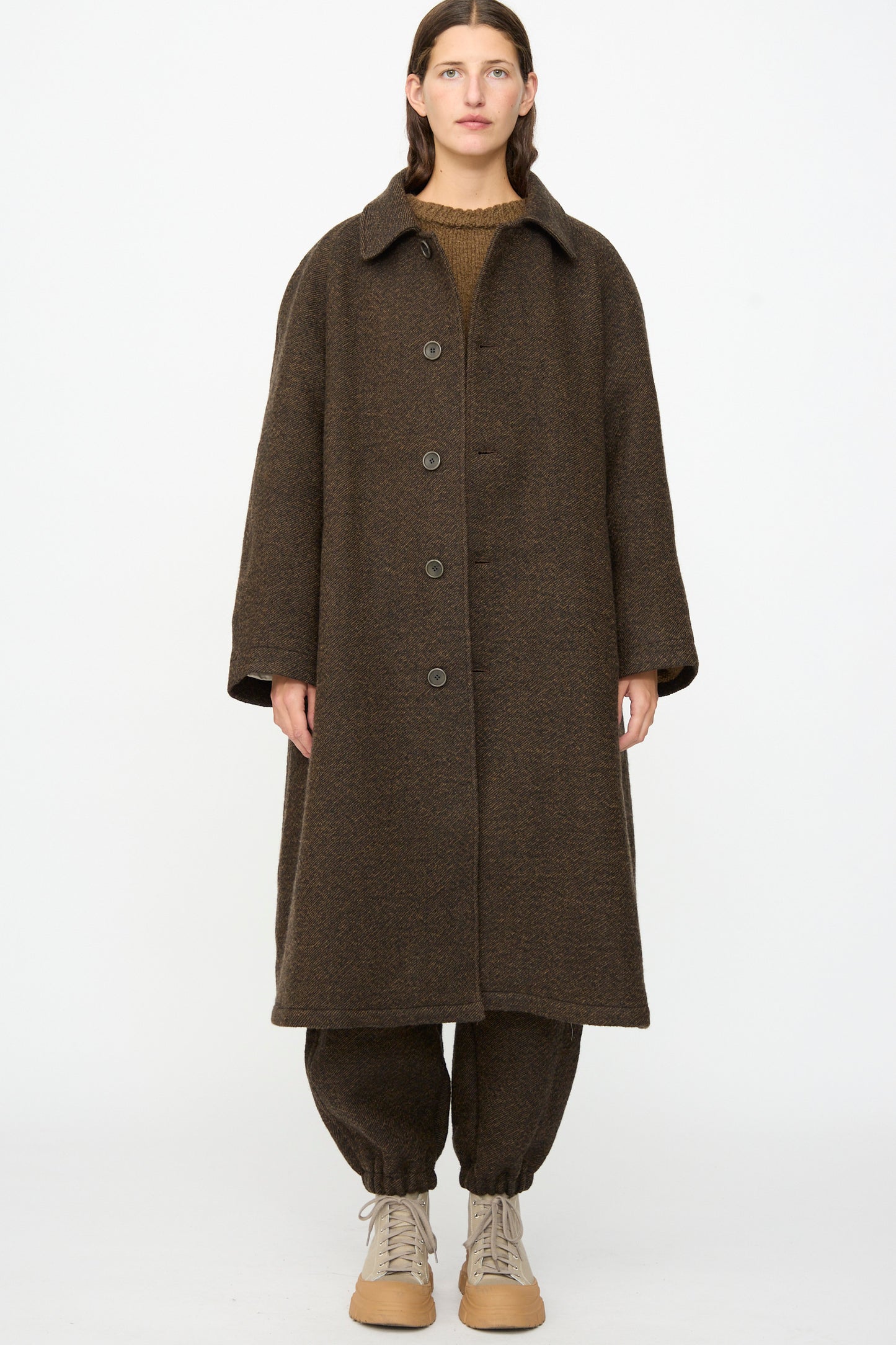 A person stands facing forward, wearing the SONO Carl Coat in Blackmud, matching brown pants, and beige boots against a plain white background.