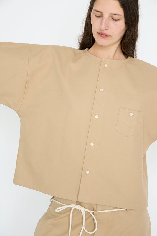 A person stands against a plain background wearing SONO's Cotton Sheldon Shirt in Jute, made  from organic cotton, arms outstretched. 