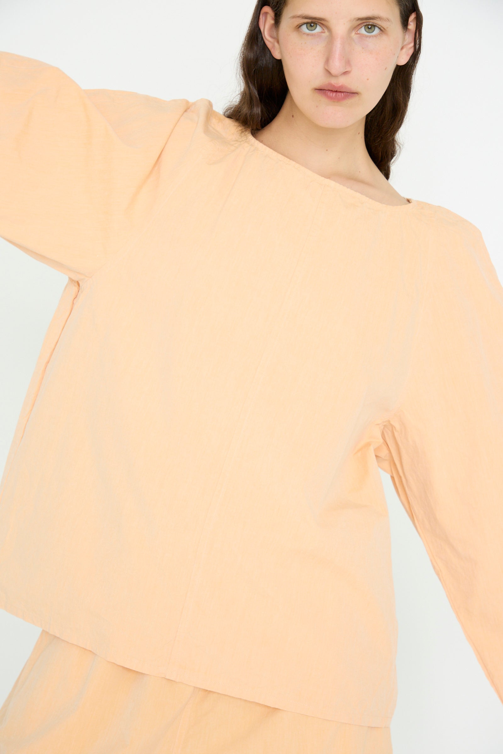 A person in a dusty peach SONO Cotton Tiga Top with organic cotton matching pants stands against a plain white background, arms slightly raised.