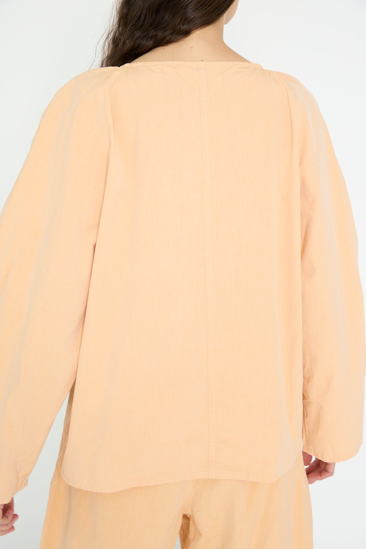 A person with long hair is seen from the back, wearing the SONO Cotton Tiga Top in Dusty Peach and matching pants. 