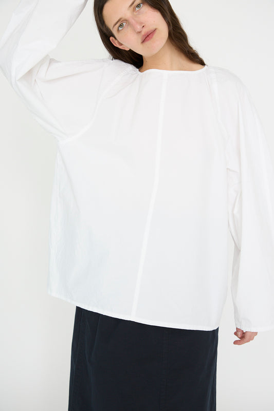 A person stands against a plain white background, clad in SONO's Cotton Tiga Top in White and a black skirt.