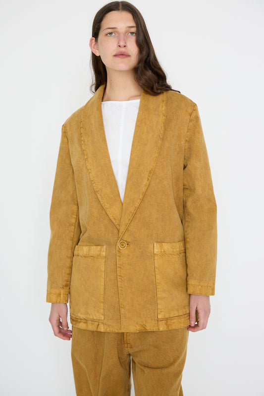 A person with long brown hair is wearing SONO's Cotton Yoyogi Jacket in Gold Clay against a plain white background, along with pants made from natural dyed fabric.