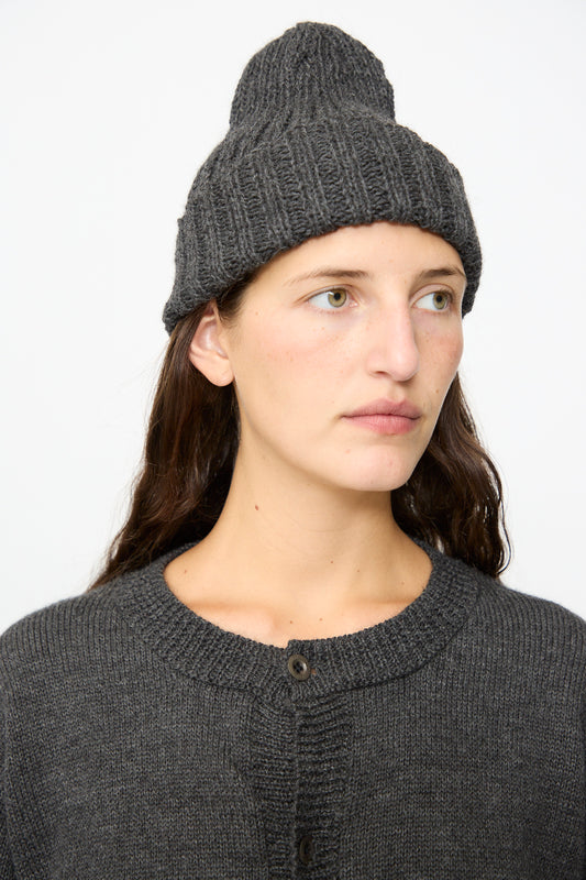 Person with long brown hair wearing the SONO Gyu Beanie in Charcoal—a cozy wool alpaca beanie made in the UK—paired with a dark gray ribbed sweater, looking slightly to the side against a plain white background.