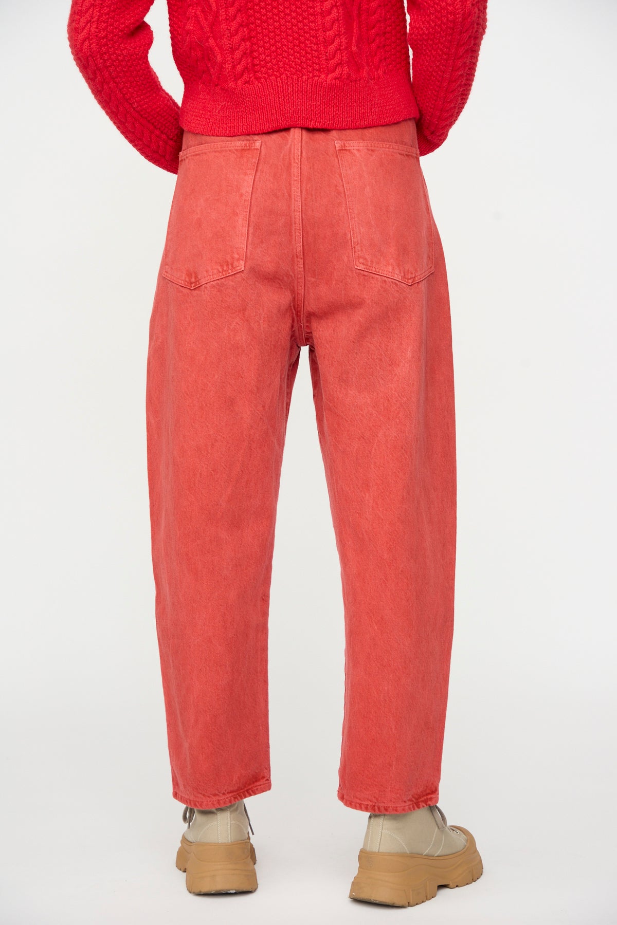 A person wearing a red sweater, SONO Jah Jeans in Red, and beige shoes, photographed from behind against a plain white background.